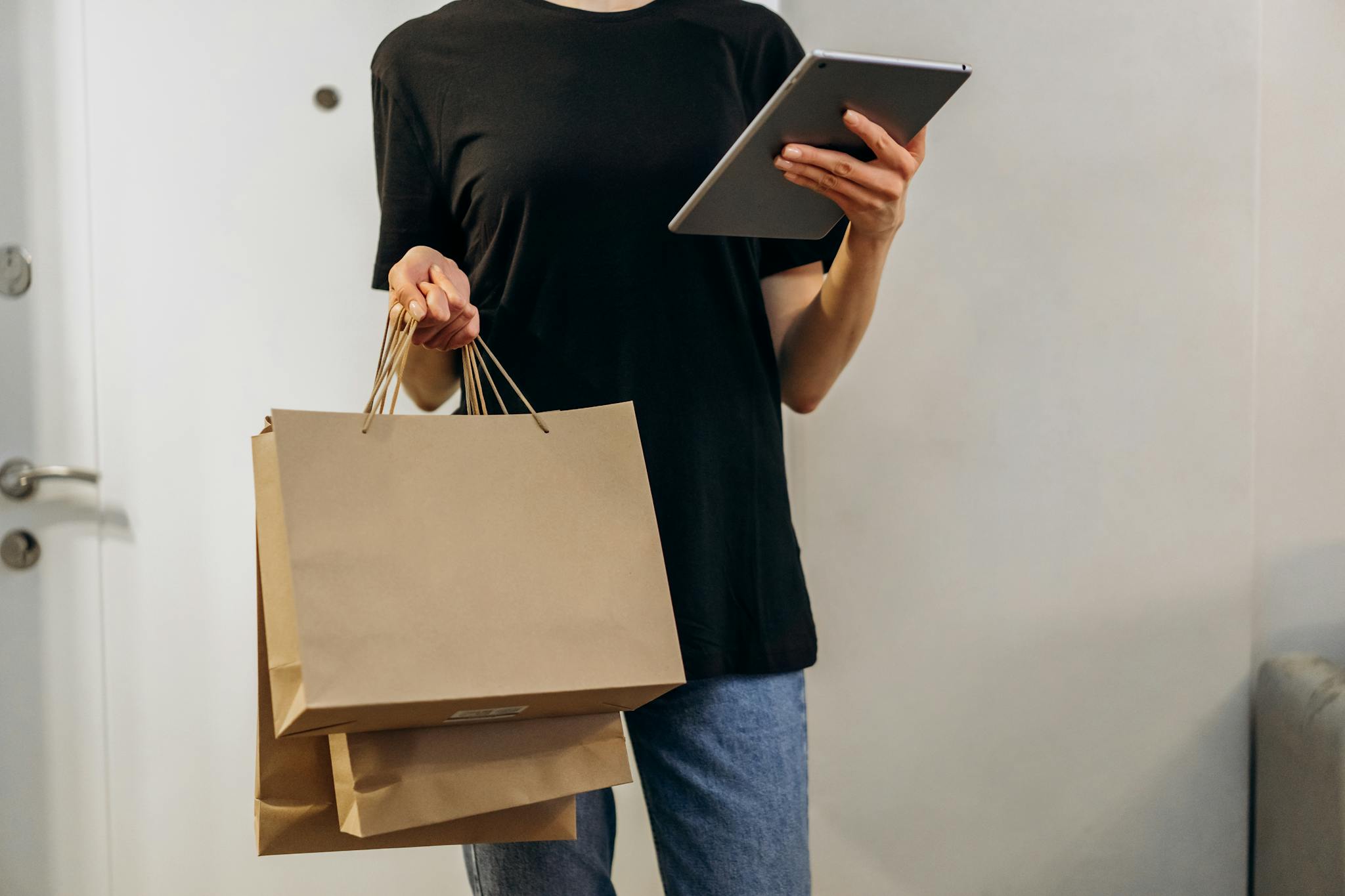 Woman in black shirt with shopping bags using a tablet at home, symbolizing online shopping convenience.